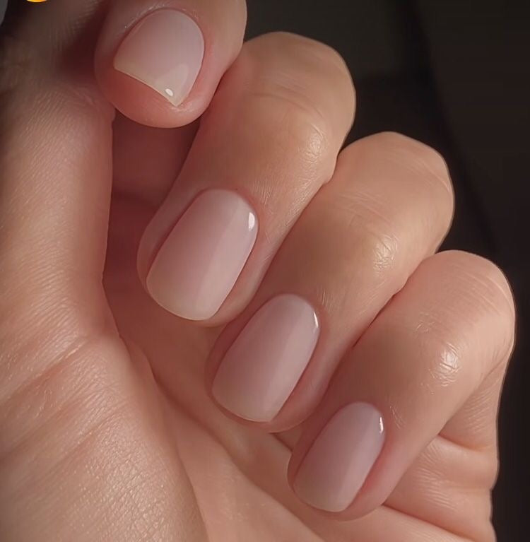 A close-up of a hand with neatly manicured nails painted in a glossy, soft nude pink color.